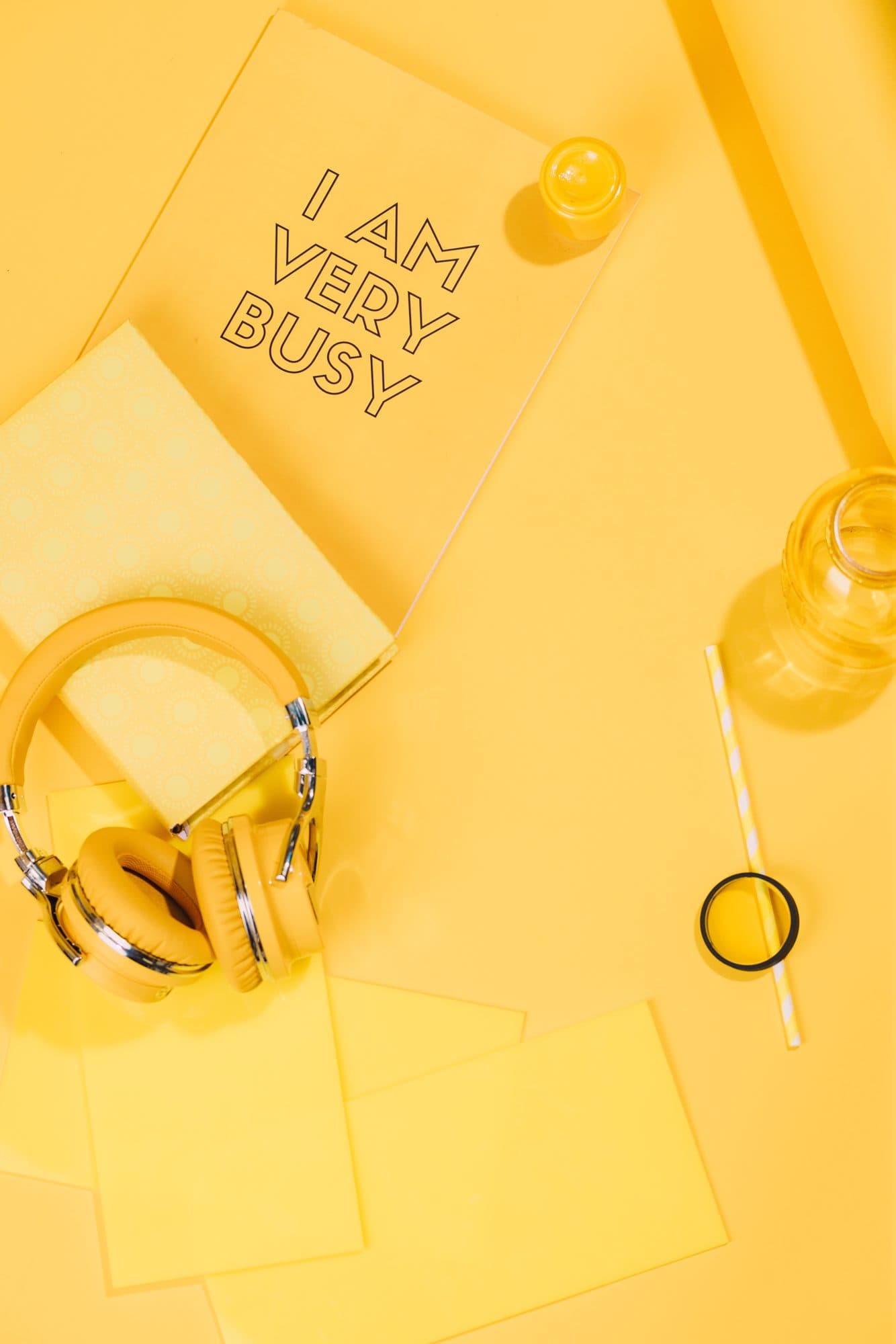 Monochrome yellow flat-lay: headphones, a notebook reading I AM VERY BUSY, a striped straw