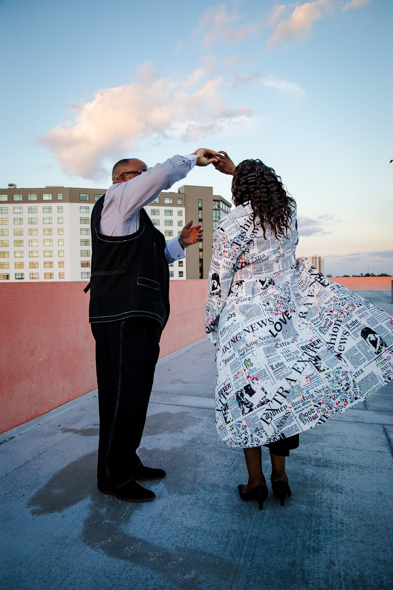 A couple dancing on a rooftop at sunset, city behind them