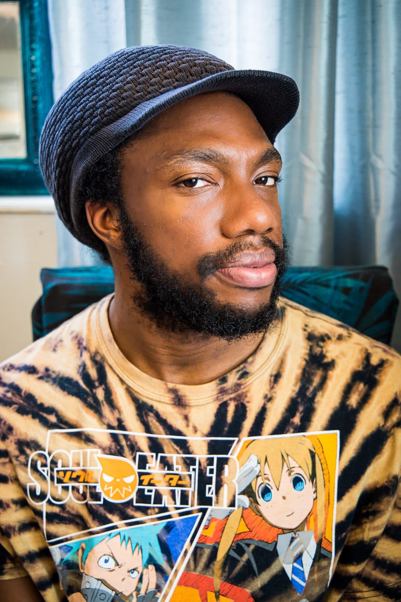 A man in a knit cap and anime tee looking straight into the lens