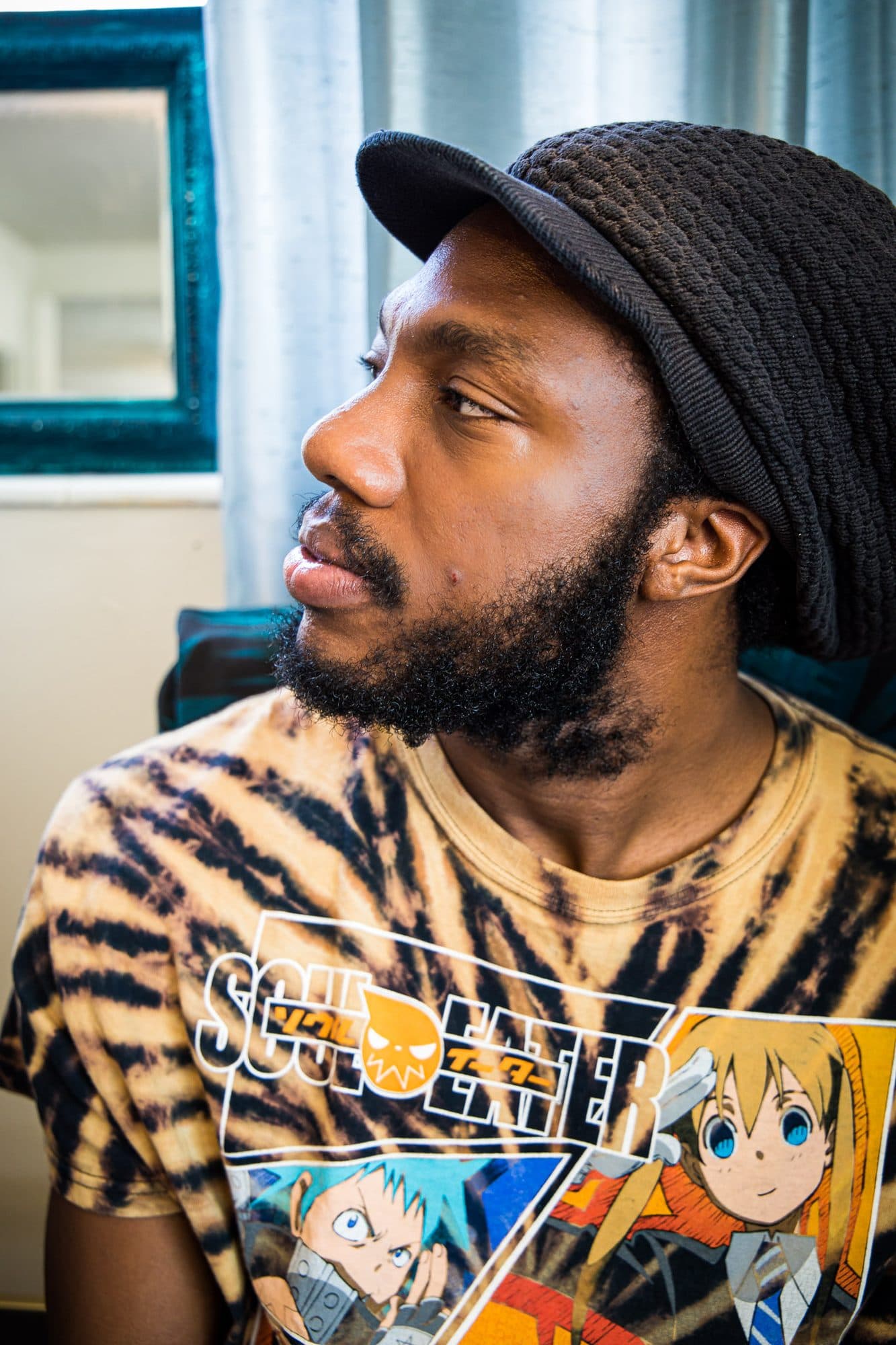 Profile of a man in a knit cap and anime tee, looking off frame