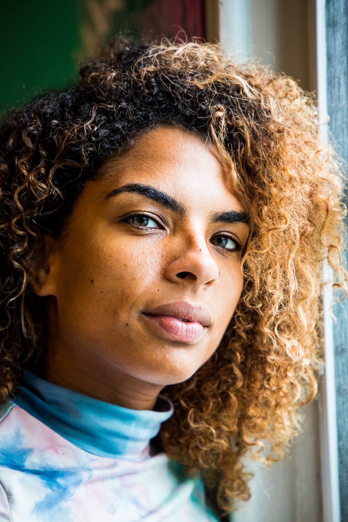 Close portrait of a woman with blonde-tipped curls in soft window light