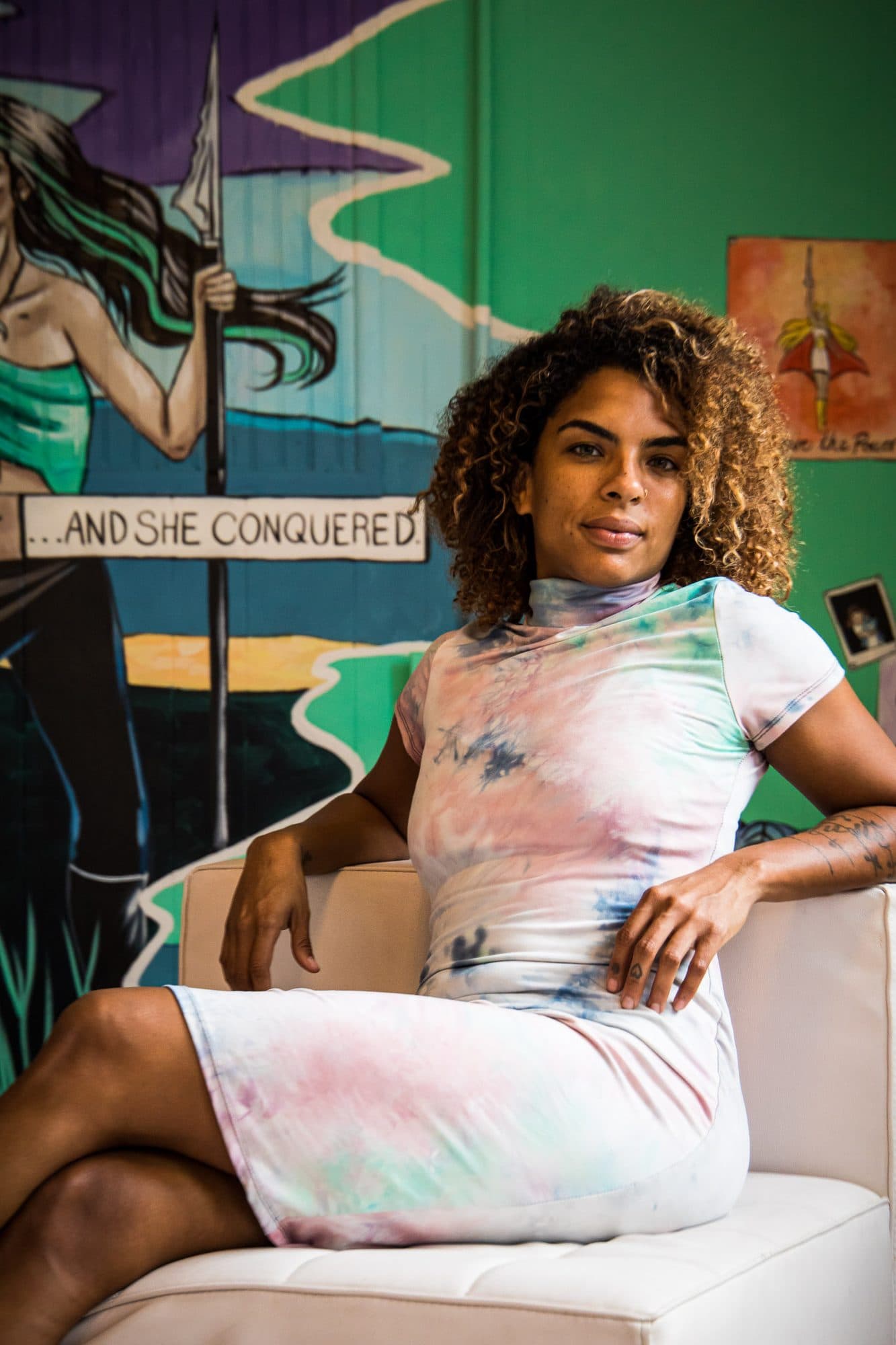 A woman in tie-dye seated beneath a painted warrior mural