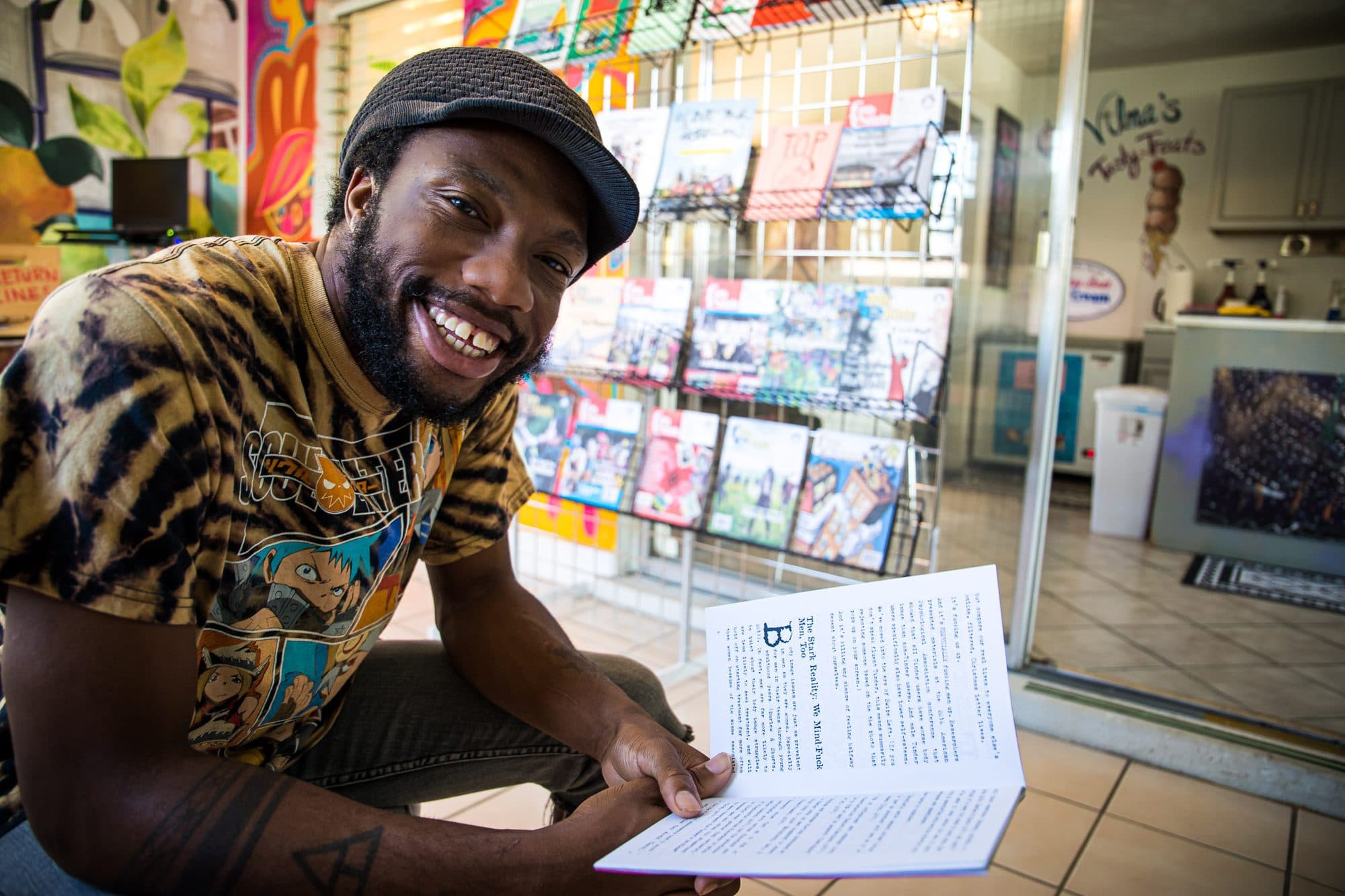 A man in tie-dye reading at a counter, smiling
