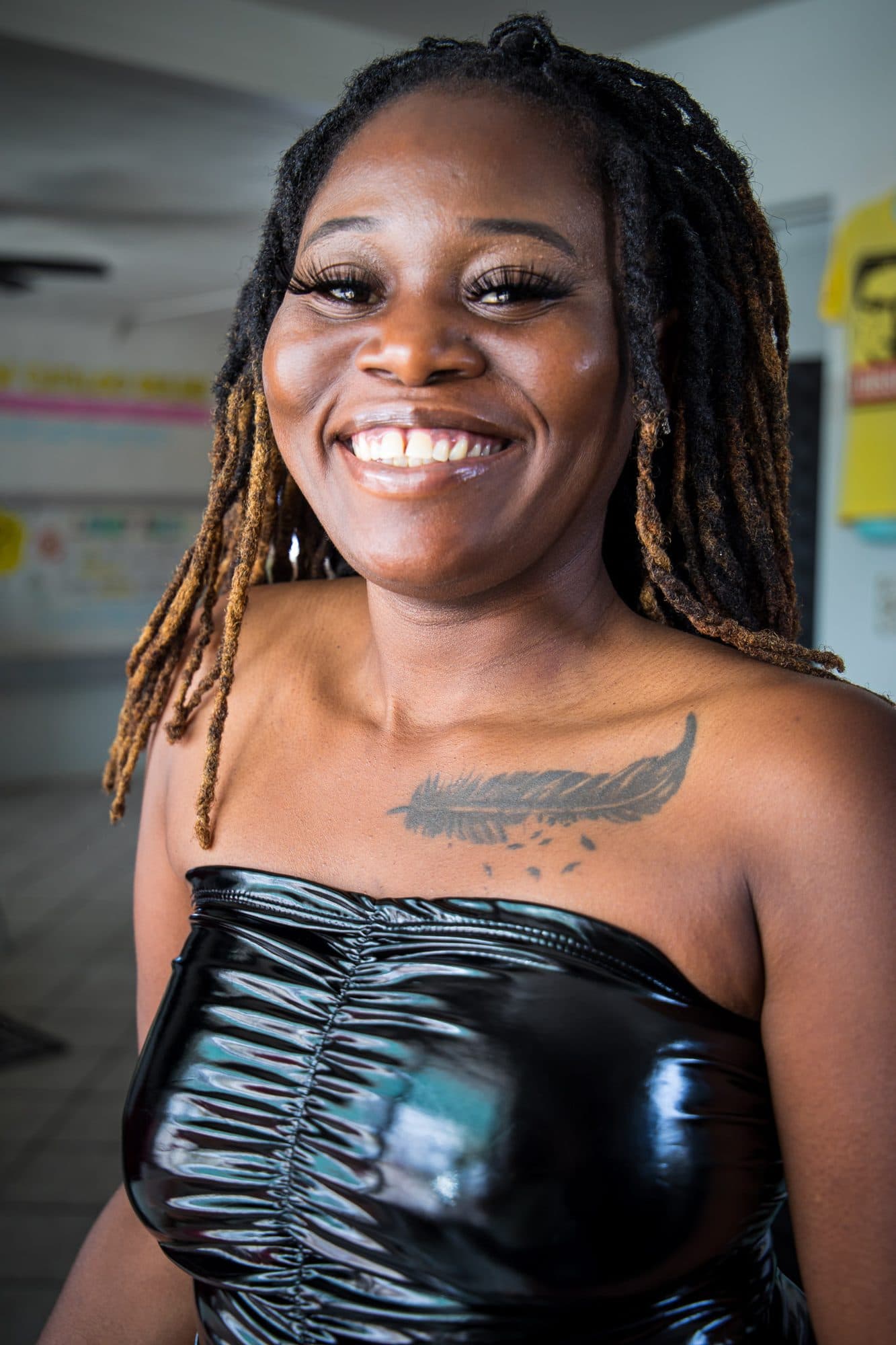 A woman in black vinyl laughing, tattoo on her shoulder