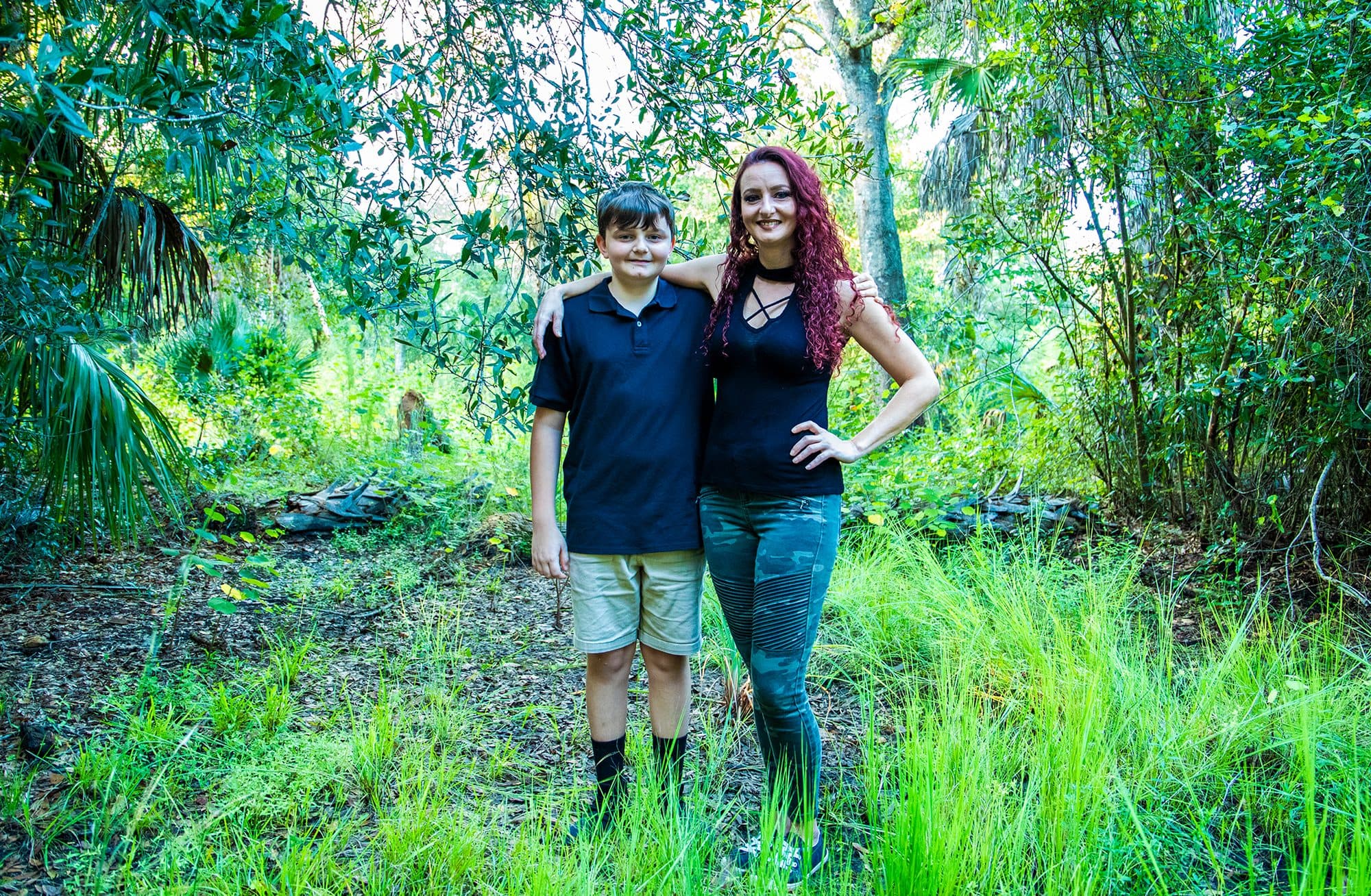 Mother and son standing together in tall grass, late sun behind the trees