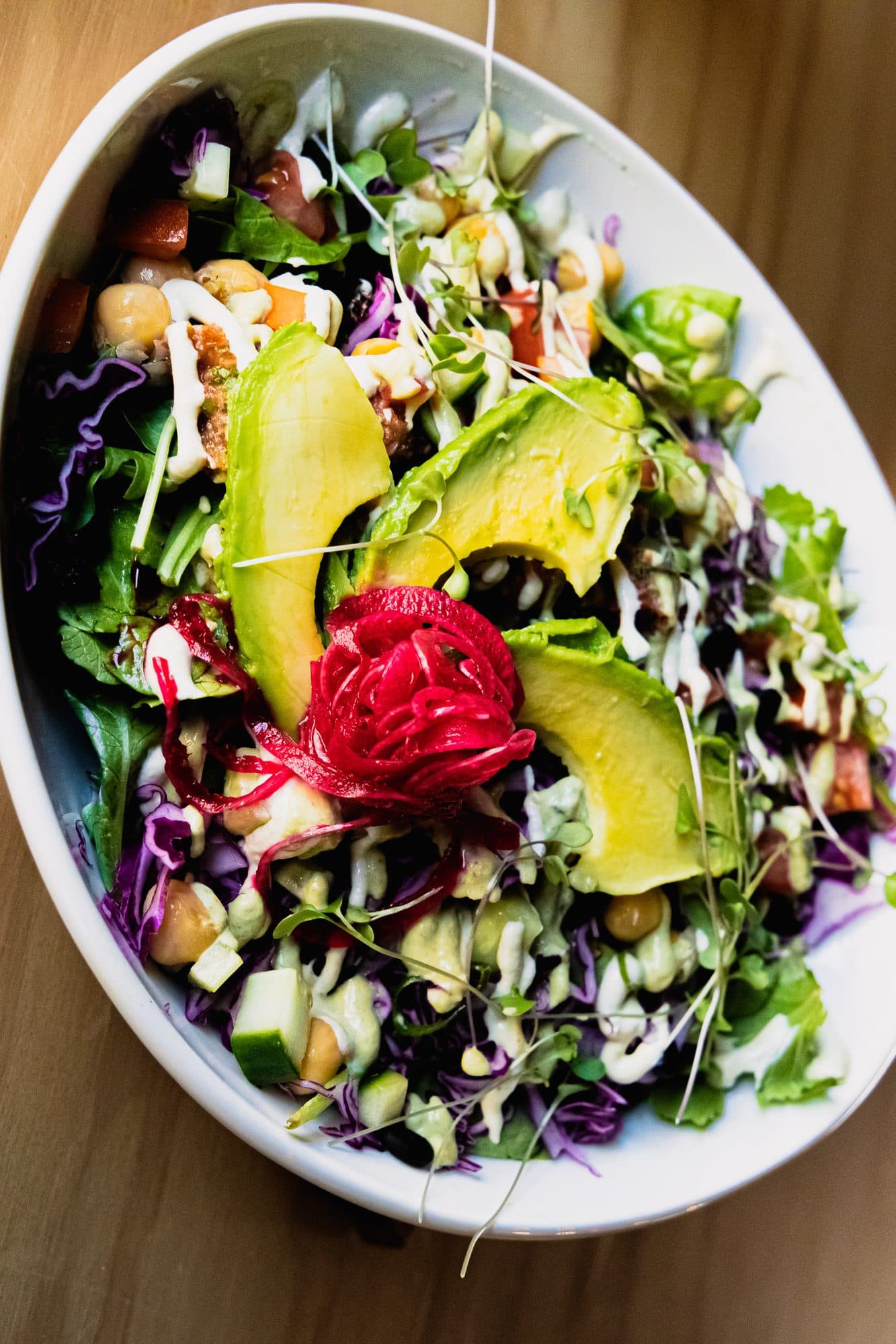 Overhead of a salad bowl with avocado, pickled onion and greens on white marble