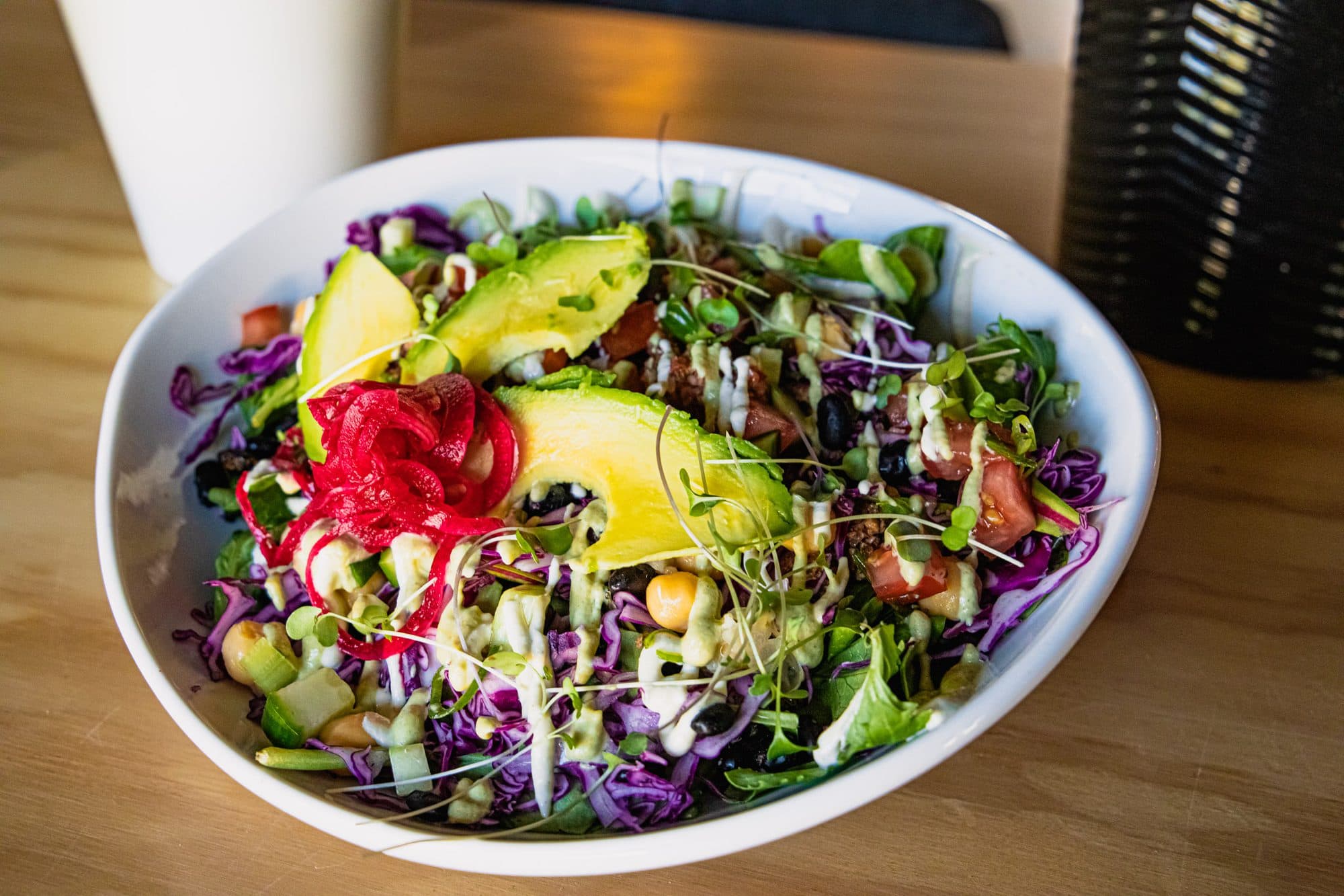 A salad bowl with avocado and pickled onion on a wood table