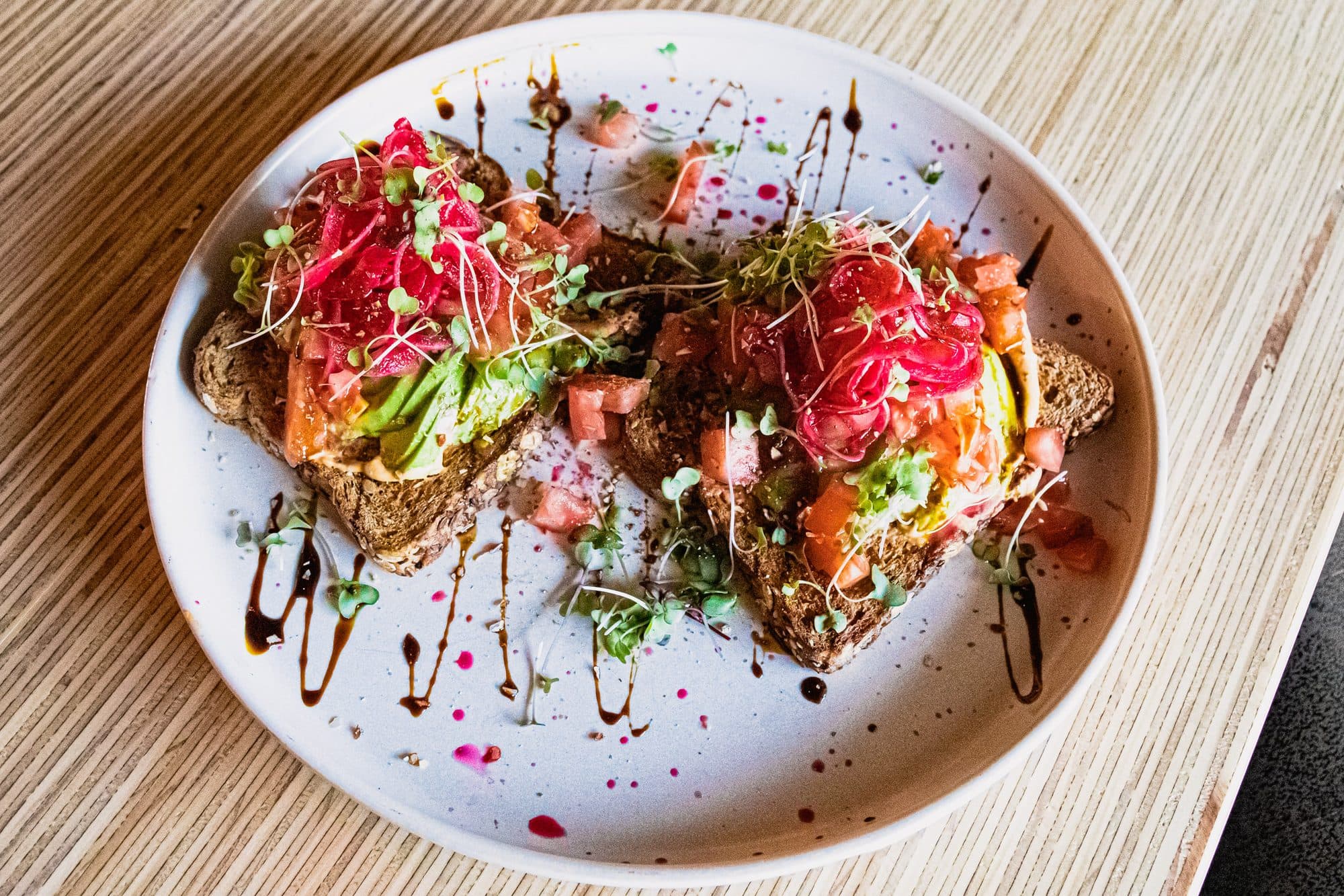 Avocado toast piled with radish and microgreens on a splattered white plate