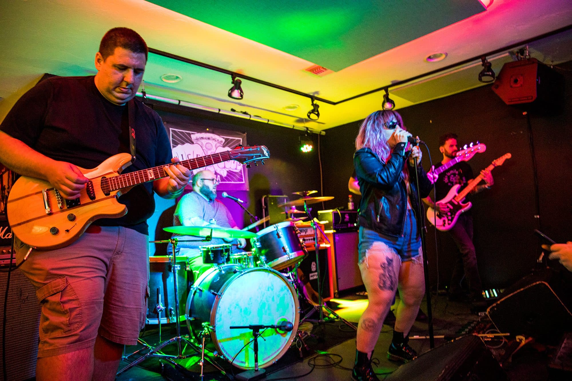Guitarist under rainbow stage lights with the band behind him