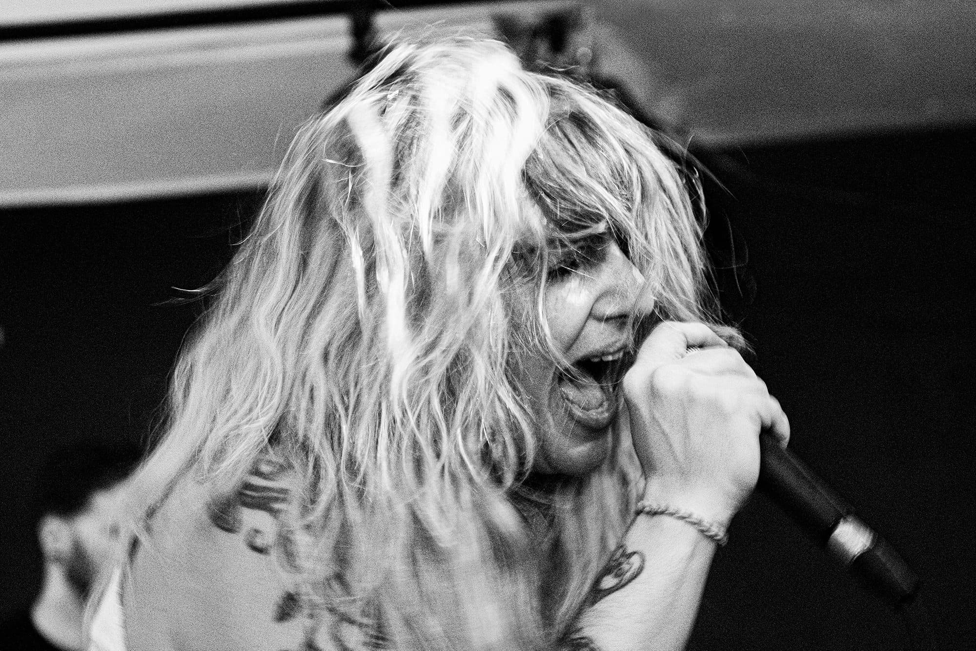 Black-and-white frame of a singer mid-scream into the microphone, hair flying