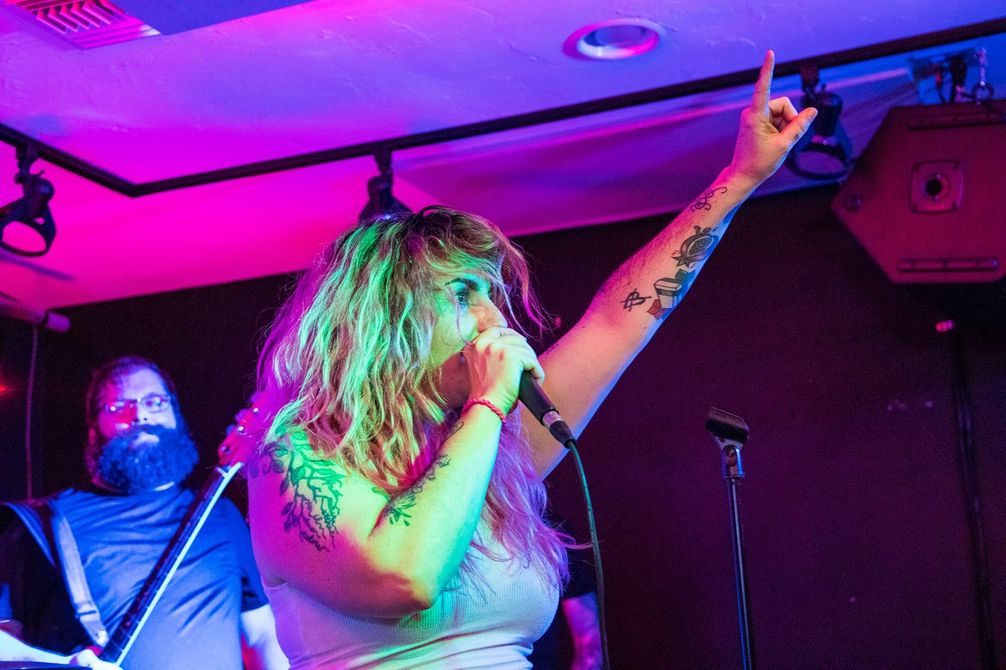 Singer pointing skyward under magenta light