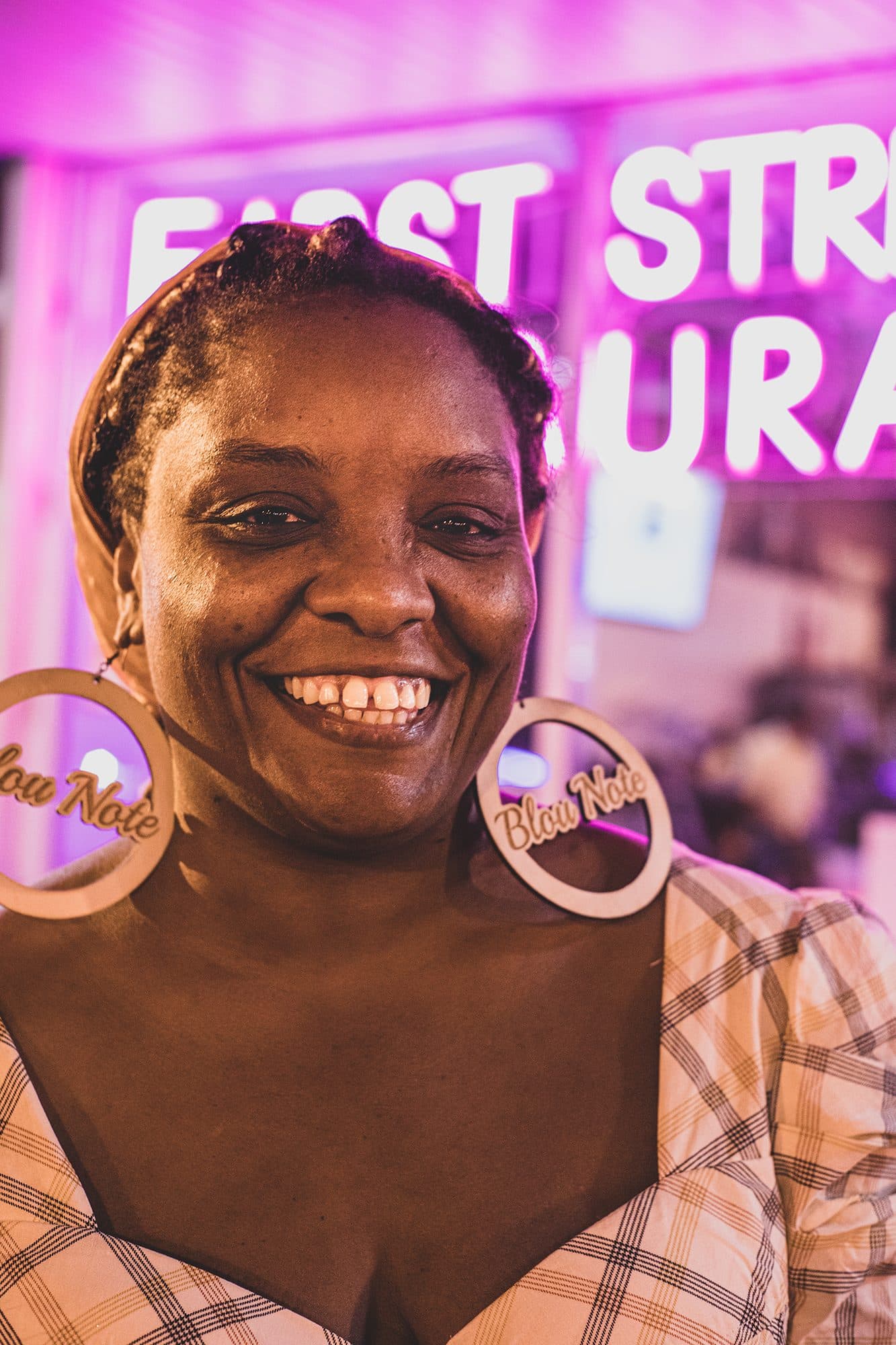 A smiling woman with hoop earrings in front of a pink neon sign