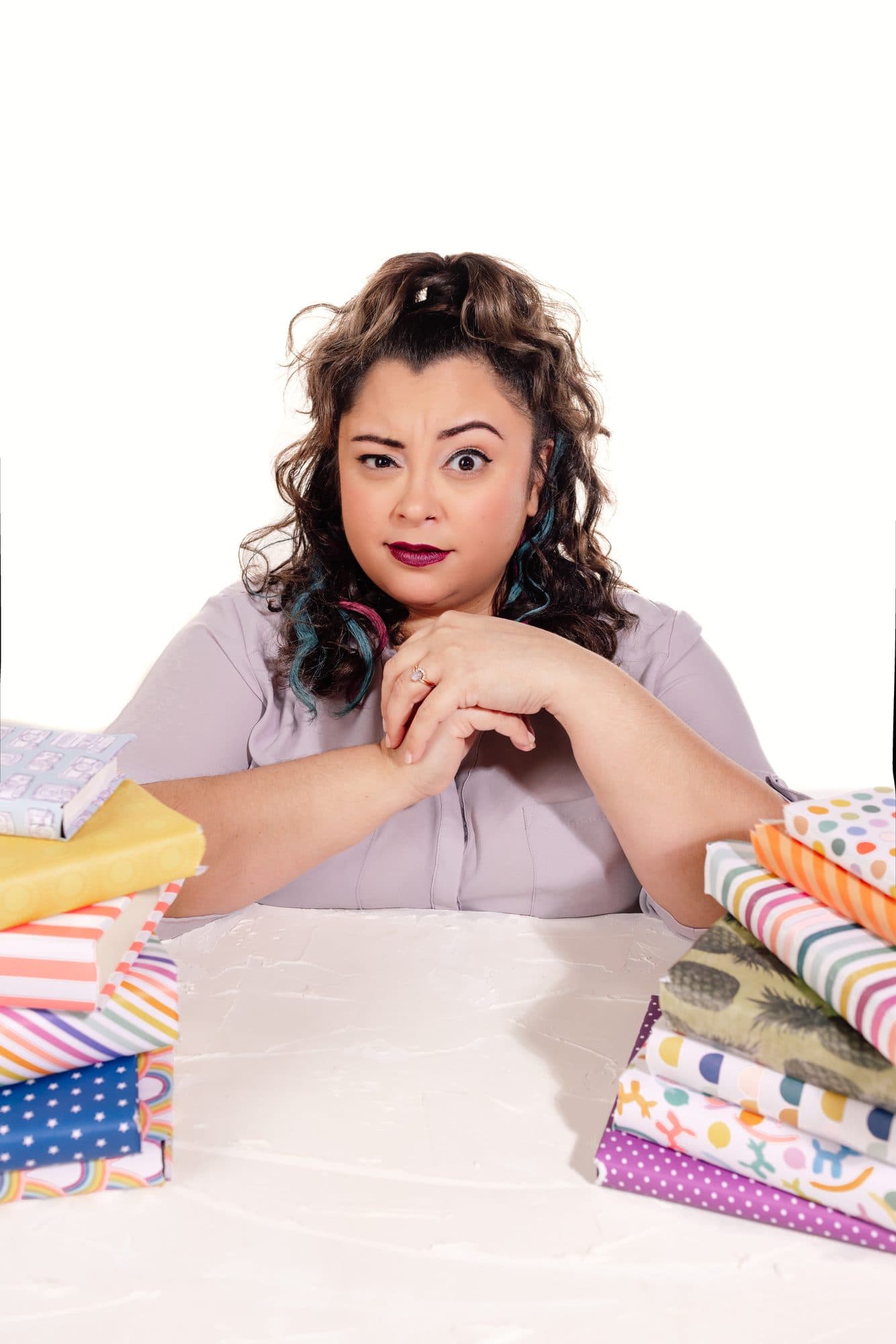 Tylor raising one eyebrow at a white table stacked with patterned books