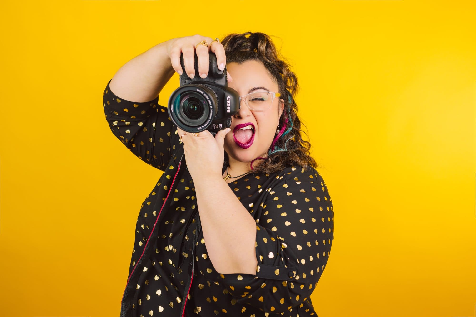 Tylor in a gold heart-print blouse, shooting straight into the lens against a mustard backdrop